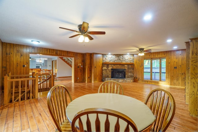 dining space featuring wooden walls, ceiling fan, stairs, a textured ceiling, and light wood-type flooring