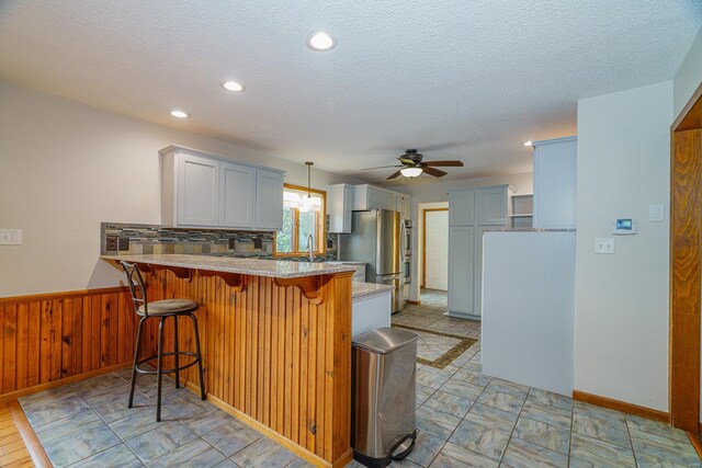 kitchen featuring a wainscoted wall, freestanding refrigerator, a peninsula, wood walls, and a kitchen bar