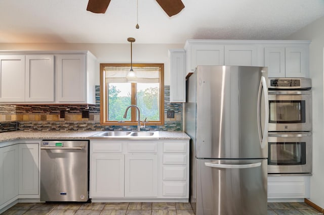 kitchen with decorative light fixtures, a sink, stainless steel appliances, white cabinetry, and backsplash