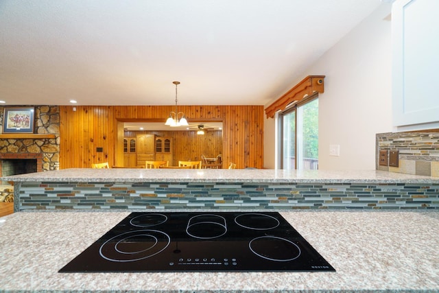 kitchen with decorative backsplash, an inviting chandelier, black electric cooktop, a fireplace, and pendant lighting