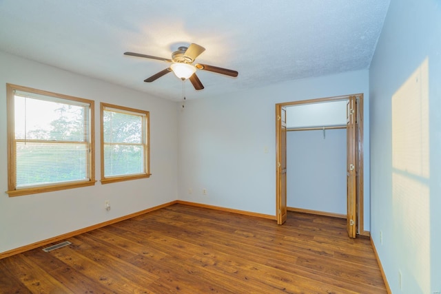 unfurnished bedroom with ceiling fan, visible vents, baseboards, a closet, and hardwood / wood-style floors