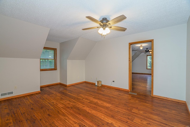 additional living space with a textured ceiling, hardwood / wood-style flooring, vaulted ceiling, and visible vents