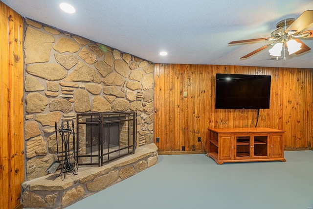 living area with a ceiling fan, wood walls, a fireplace, and a textured ceiling