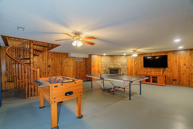 game room with concrete flooring, ceiling fan, a textured ceiling, wood walls, and a fireplace