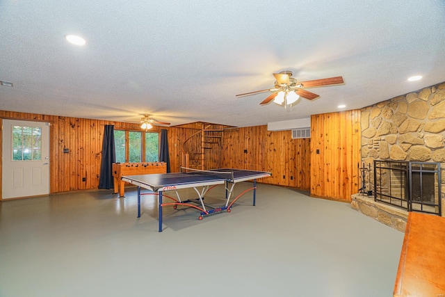 recreation room with finished concrete flooring, wood walls, a textured ceiling, and a stone fireplace