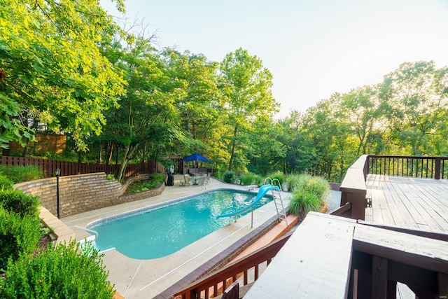 view of pool featuring a patio, a water slide, fence, a wooden deck, and a fenced in pool