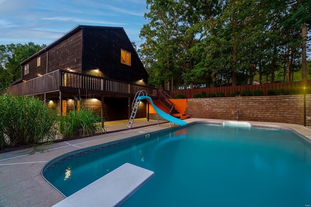 view of swimming pool featuring a fenced in pool, fence, a water slide, a wooden deck, and a diving board