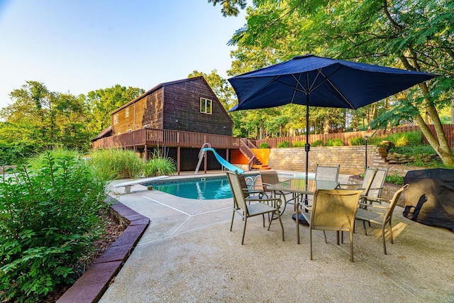 view of swimming pool featuring a patio, outdoor dining space, fence, a water slide, and a diving board