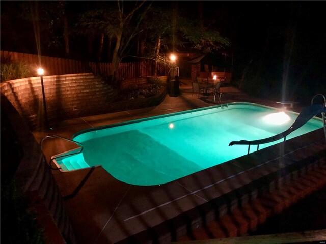 pool at twilight featuring a patio area, fence, an indoor pool, and a water slide