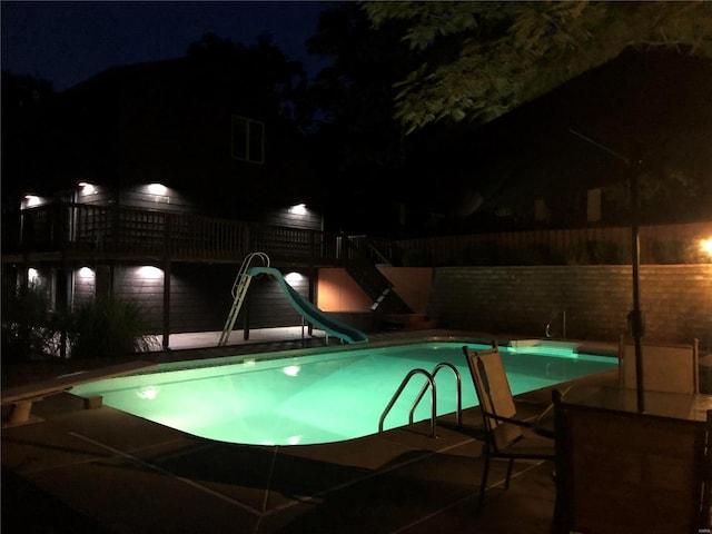 pool at night featuring a patio area, a fenced in pool, fence, and a water slide