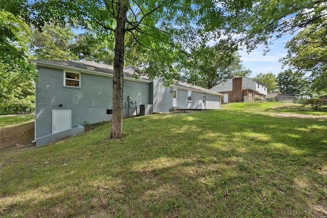 rear view of property with a garage, a yard, brick siding, and central AC unit