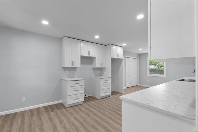 kitchen with recessed lighting, a sink, baseboards, white cabinets, and light wood-type flooring