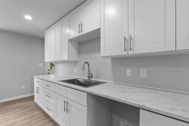 kitchen featuring light wood-type flooring, white cabinetry, light stone counters, and sink