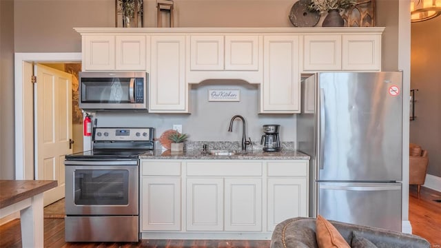 kitchen featuring stainless steel appliances, hardwood / wood-style floors, white cabinets, sink, and light stone counters