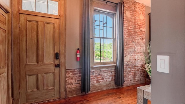 foyer entrance featuring brick wall and wood-type flooring