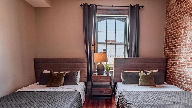 bedroom featuring brick wall and dark hardwood / wood-style flooring