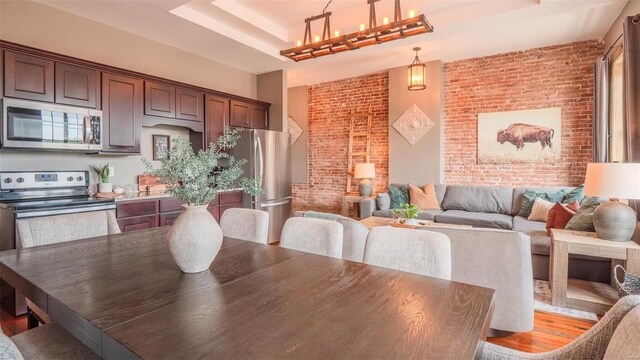 dining room with brick wall, a high ceiling, light wood-type flooring, and a tray ceiling