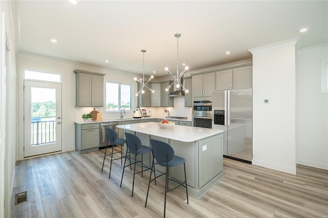 kitchen with appliances with stainless steel finishes, a kitchen breakfast bar, gray cabinetry, light hardwood / wood-style flooring, and a center island