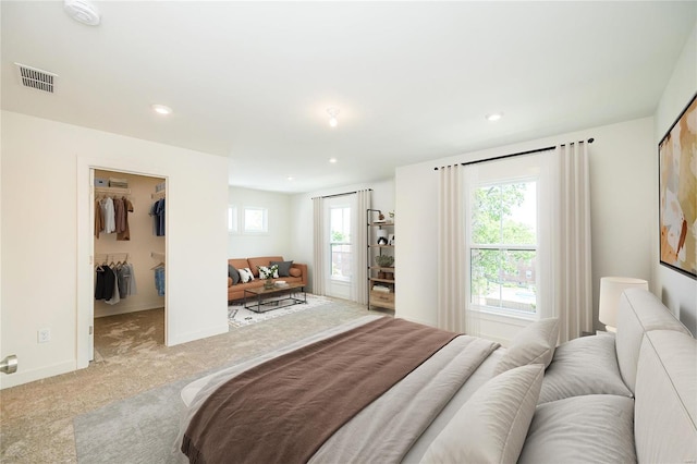 bedroom with a walk in closet, light colored carpet, and a closet