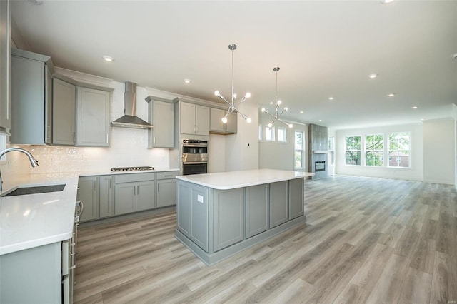 kitchen featuring double oven, sink, wall chimney range hood, gray cabinets, and a kitchen island