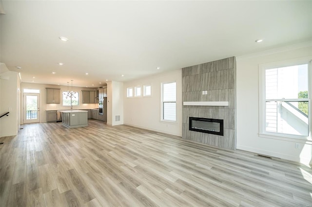 unfurnished living room with a tiled fireplace, crown molding, sink, and light hardwood / wood-style floors