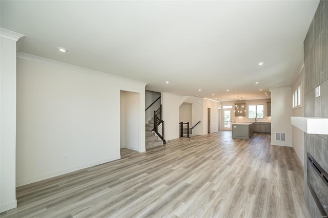 unfurnished living room with a tiled fireplace, light hardwood / wood-style flooring, an inviting chandelier, and ornamental molding