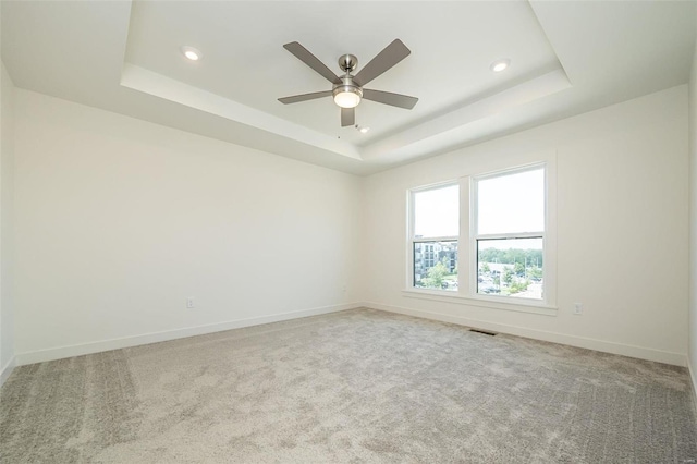 empty room with a raised ceiling, ceiling fan, and carpet