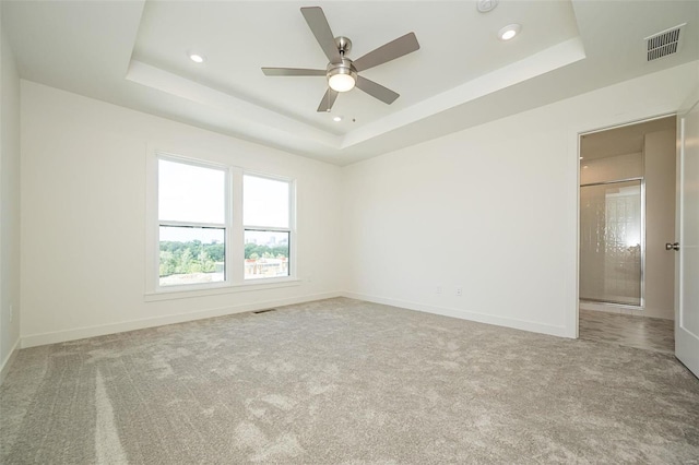 carpeted spare room with a tray ceiling and ceiling fan