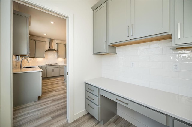 kitchen featuring gray cabinetry, wall chimney range hood, sink, tasteful backsplash, and light hardwood / wood-style floors