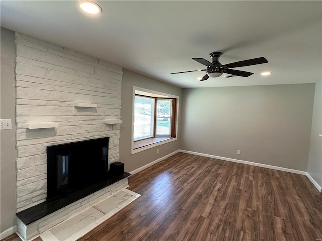 unfurnished living room featuring ceiling fan, dark hardwood / wood-style flooring, and a stone fireplace