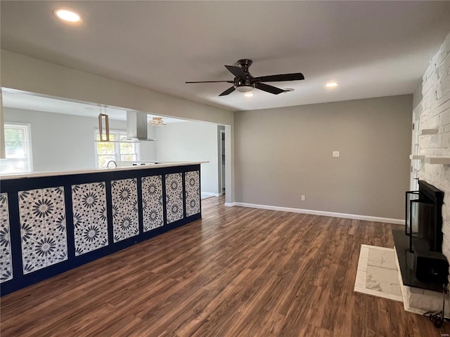 unfurnished living room featuring ceiling fan, a stone fireplace, and dark hardwood / wood-style flooring