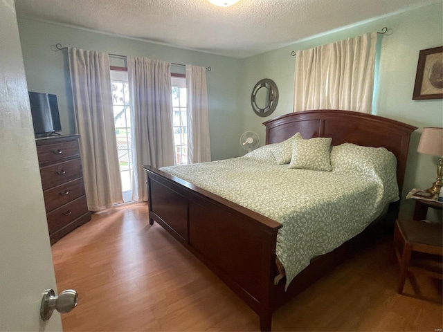 bedroom with access to outside, hardwood / wood-style flooring, and a textured ceiling