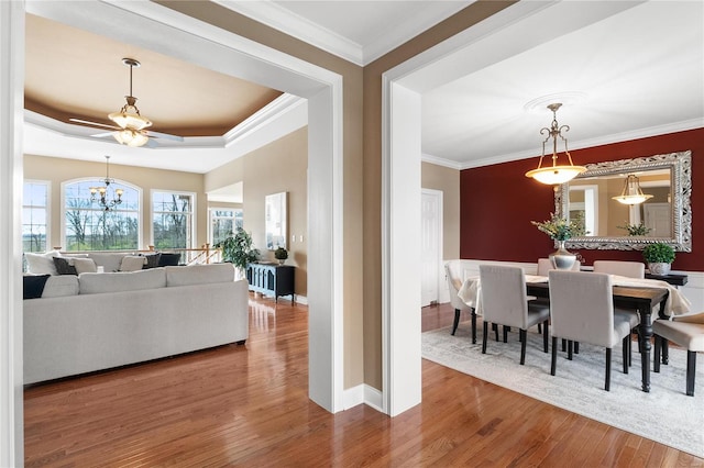 dining area with ceiling fan with notable chandelier, hardwood / wood-style flooring, a tray ceiling, and crown molding