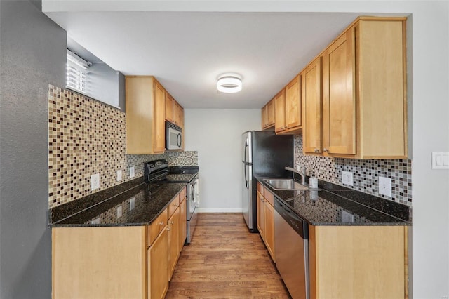 kitchen with stainless steel appliances, dark stone countertops, a sink, and light wood finished floors