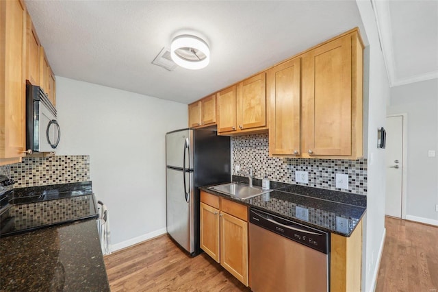 kitchen with light wood-type flooring, appliances with stainless steel finishes, dark stone counters, and a sink