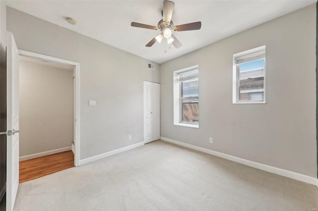 unfurnished bedroom featuring ceiling fan, light carpet, visible vents, baseboards, and a closet