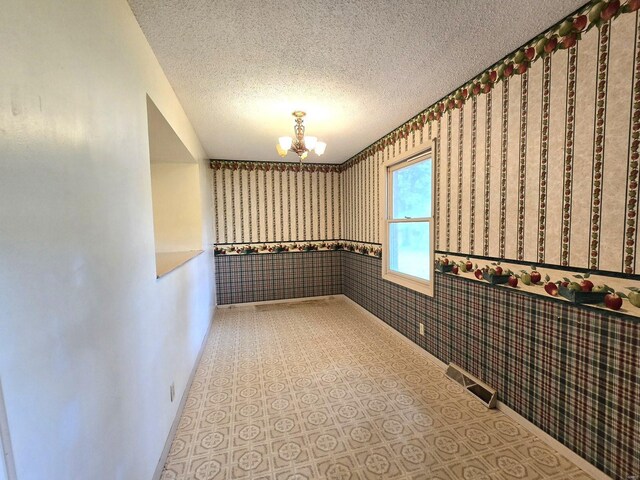 hall with a textured ceiling, a notable chandelier, and tile patterned flooring