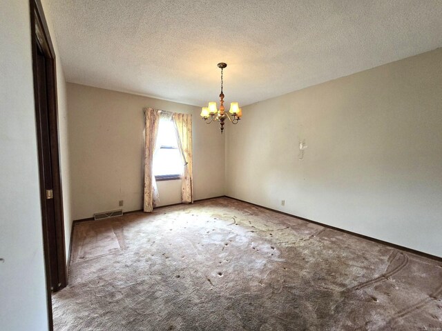 carpeted empty room featuring a textured ceiling and a chandelier