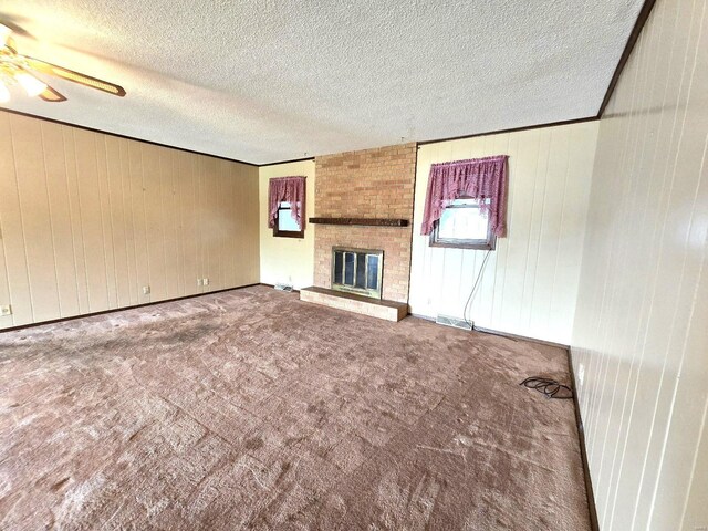 unfurnished living room with ceiling fan, a textured ceiling, brick wall, carpet floors, and a brick fireplace