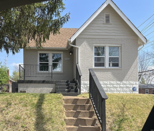 view of front facade featuring stairs, brick siding, roof with shingles, and a front yard