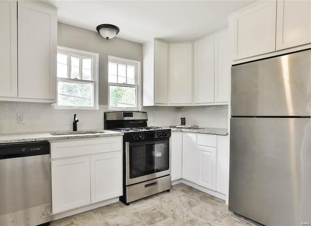 kitchen with light tile patterned flooring, stainless steel appliances, white cabinets, sink, and light stone countertops