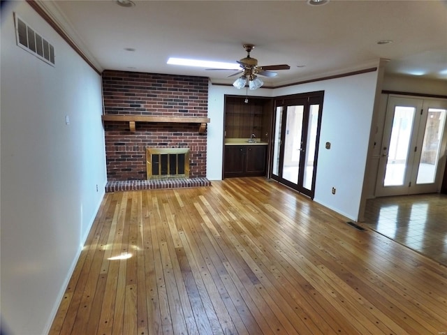 unfurnished living room with ornamental molding, hardwood / wood-style flooring, a healthy amount of sunlight, and a brick fireplace