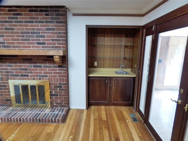 bar with crown molding, light hardwood / wood-style flooring, a brick fireplace, sink, and dark brown cabinetry