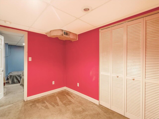 unfurnished bedroom with a drop ceiling, a closet, and carpet floors