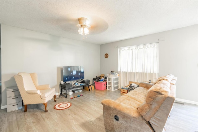 living room with a textured ceiling, ceiling fan, and light hardwood / wood-style flooring