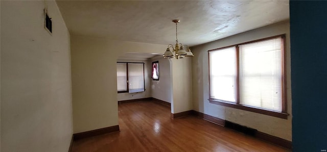 spare room with an inviting chandelier and hardwood / wood-style flooring