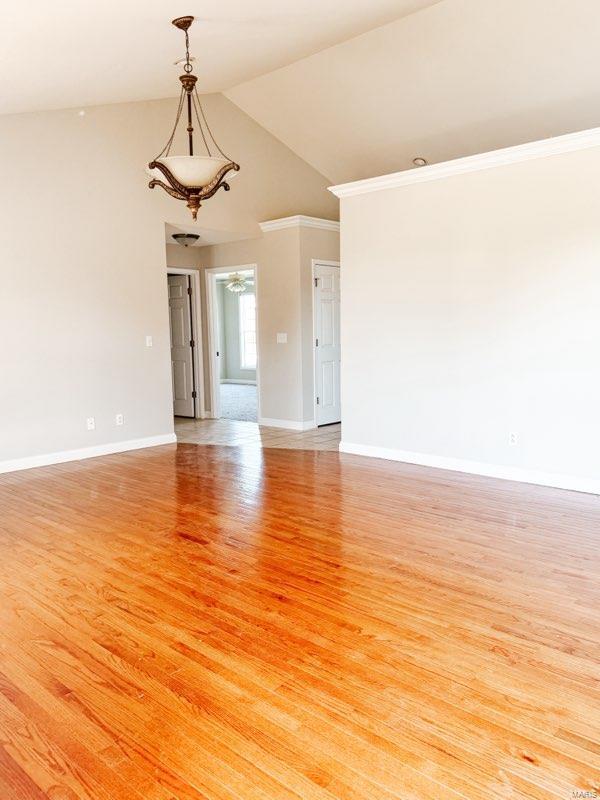 empty room with light wood-type flooring, crown molding, and vaulted ceiling