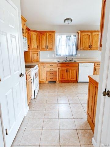 kitchen featuring light tile patterned flooring, white appliances, and sink