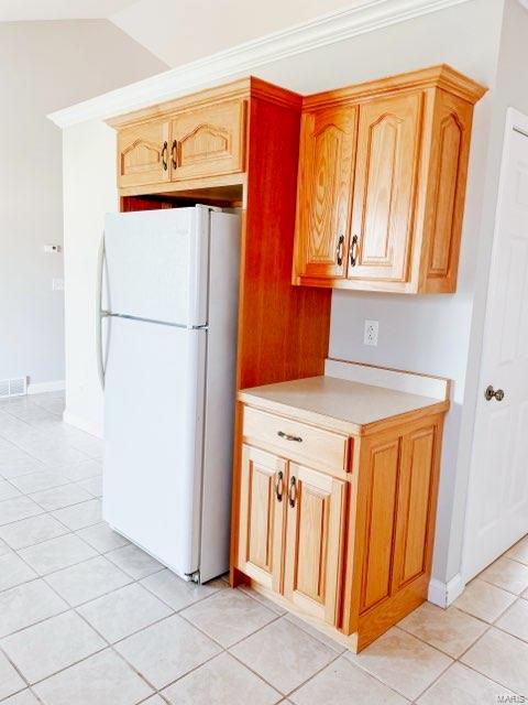 kitchen featuring white refrigerator, lofted ceiling, crown molding, and light tile patterned floors