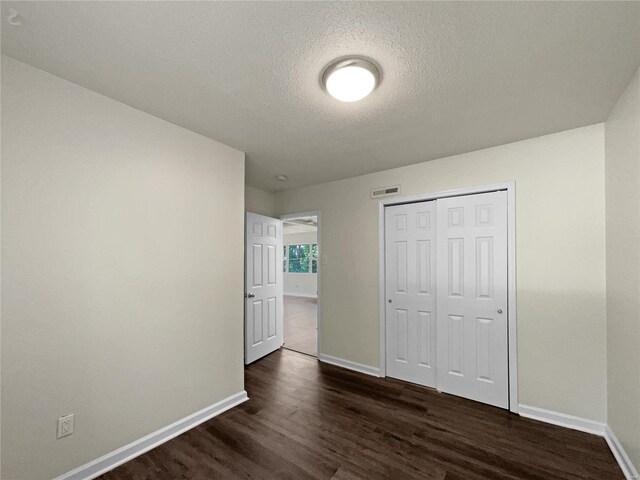 unfurnished bedroom with a closet, dark wood-type flooring, and a textured ceiling